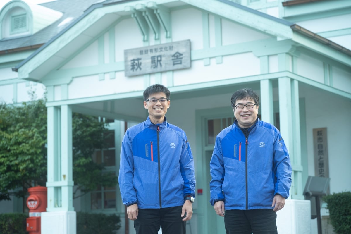 萩観光協会の専務理事・藤田将一さん（右）と、萩版DMO事業マーケティング責任者の上利寿博さん。有形文化財になっている萩駅舎前での写真。